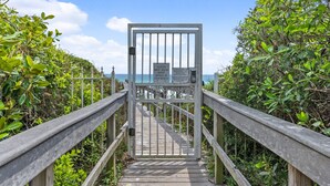 A wooden boardwalk leading to a beach with a metal gate and a sign indicating guests must wear bands at the beach.