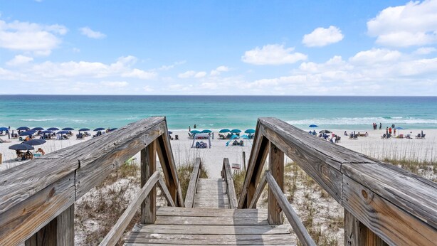 A wooden staircase leading to a beach with umbrellas and people.