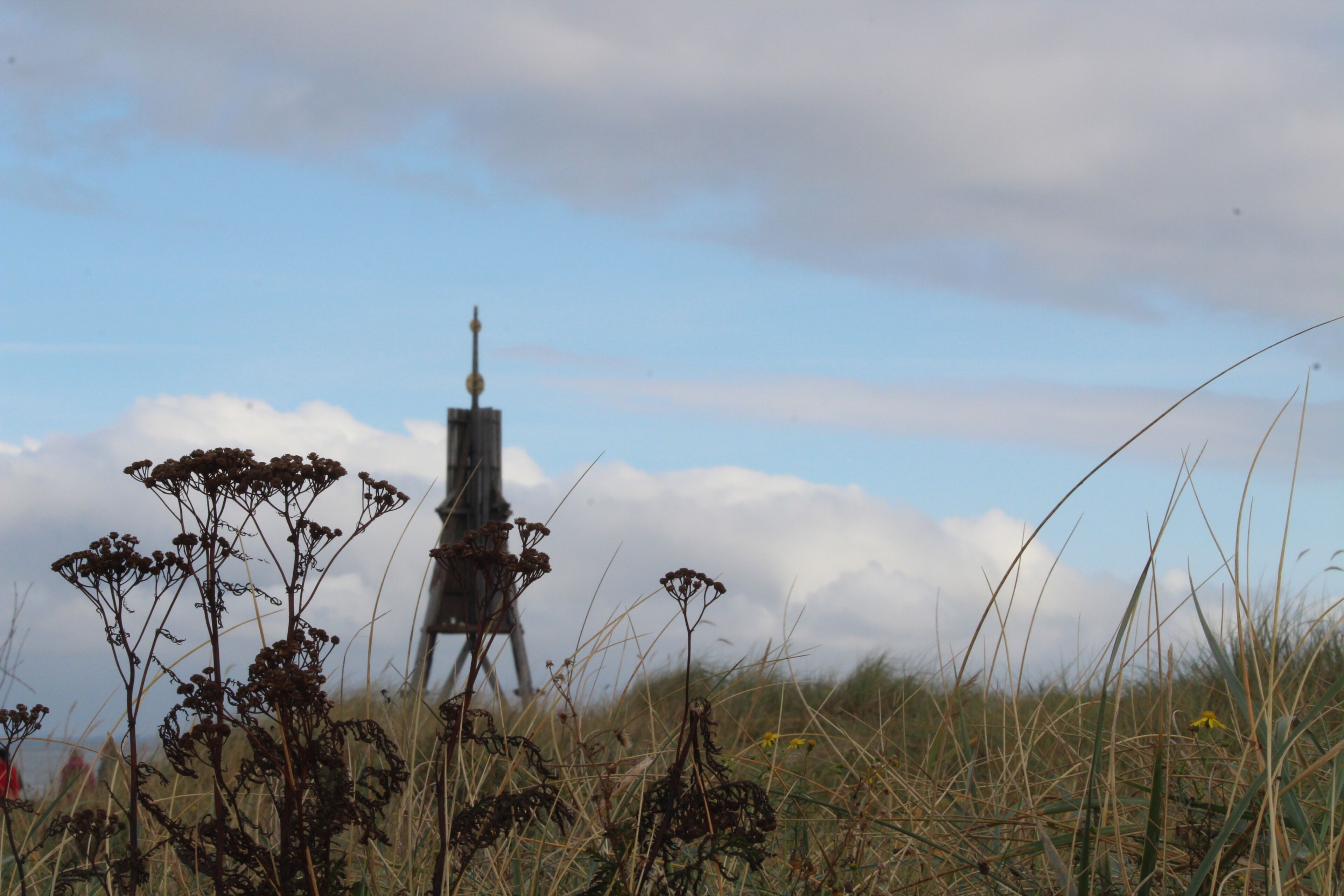 A tall, narrow tower-like structure in a grassy field with a clear sky in the background.