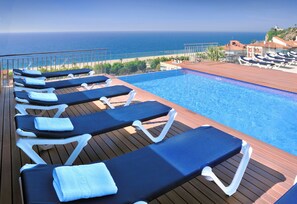 Zona junto a la piscina con sillas de descanso y vista al océano.
