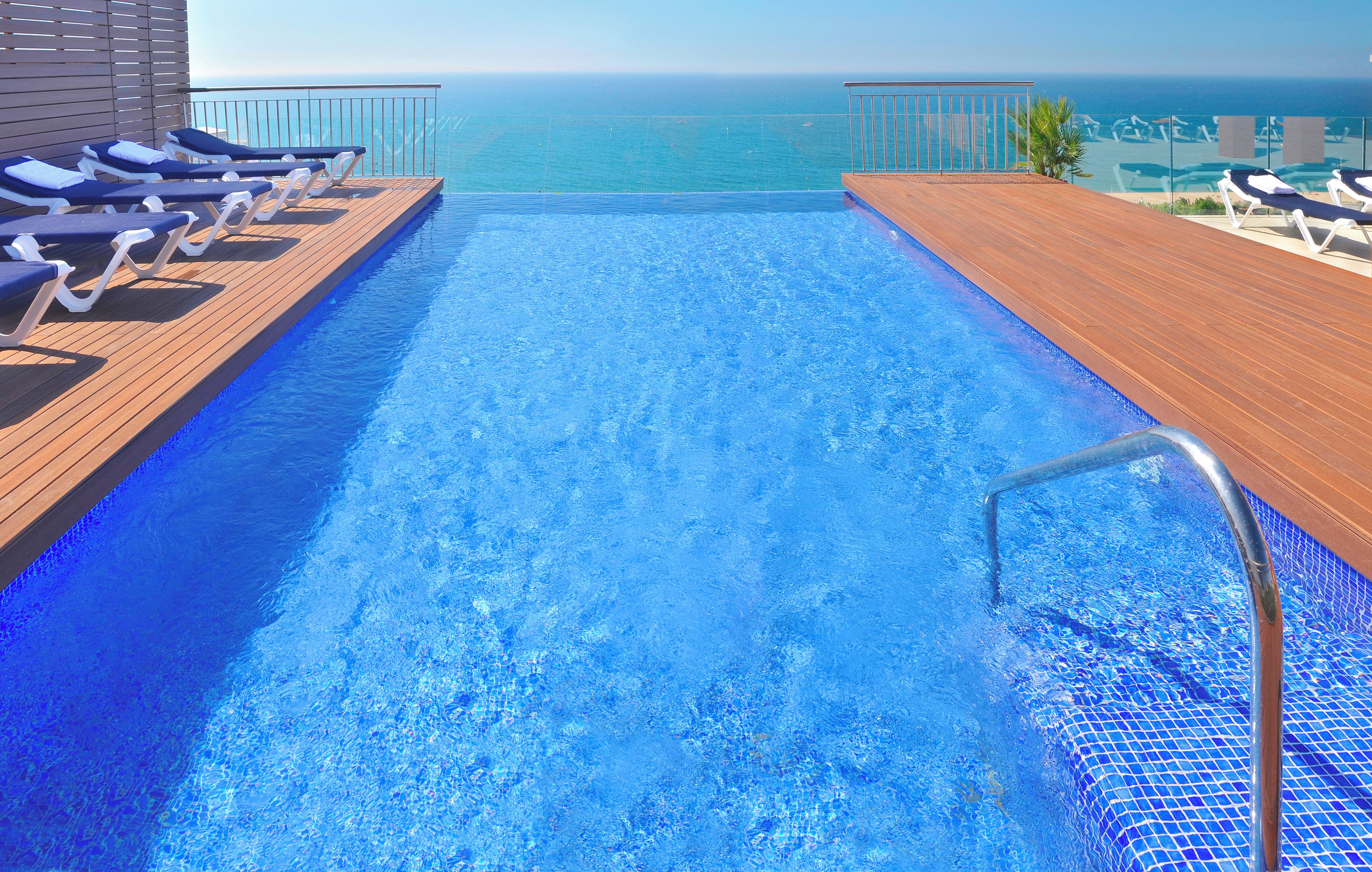 Una piscina con vista al océano, terraza de madera y sillas de descanso.