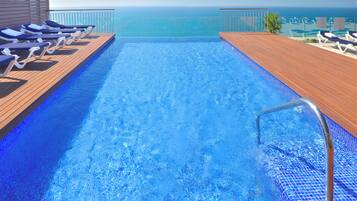 Una piscina con vista al océano, terraza de madera y sillas de descanso.