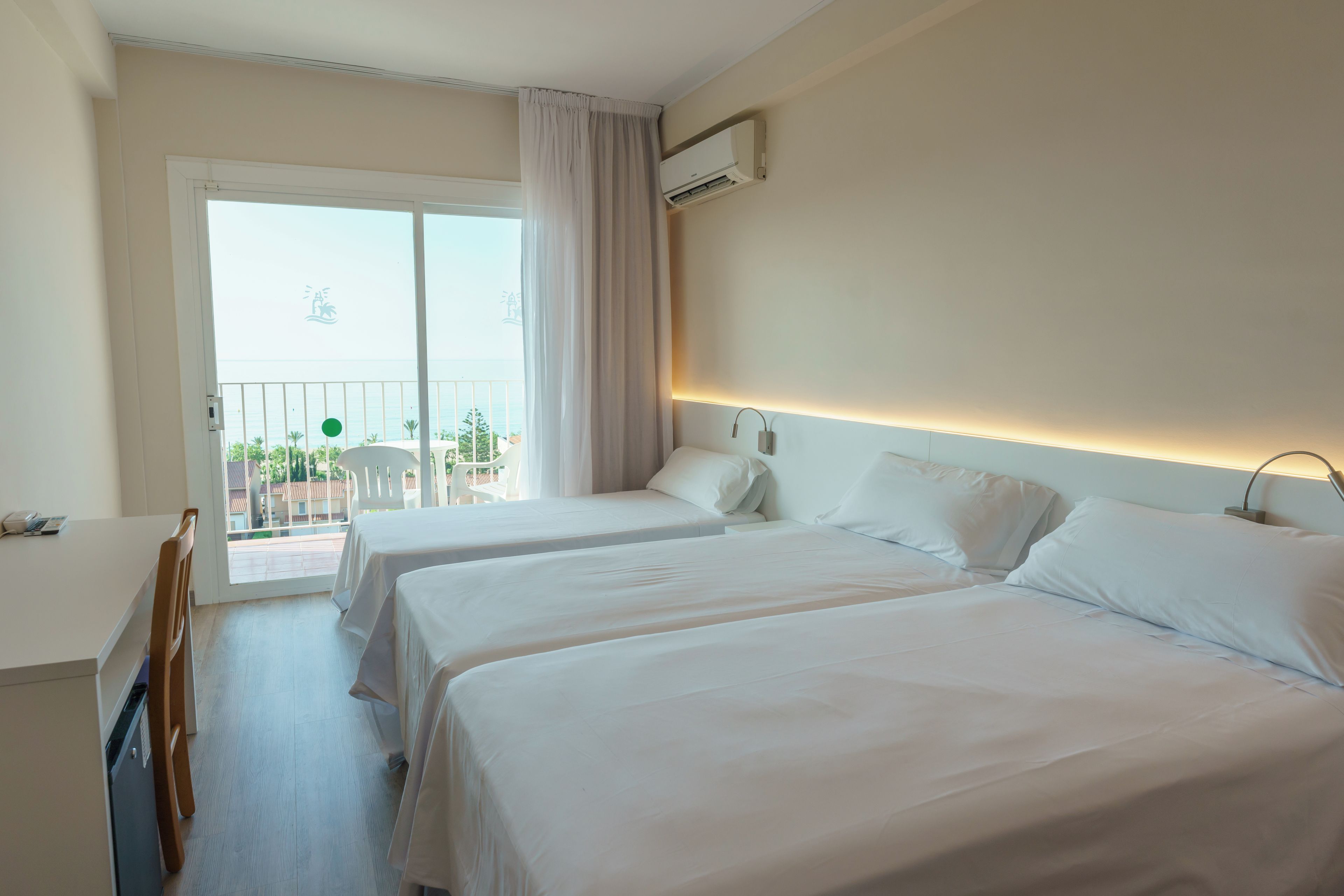 Una habitación de hotel con dos camas, un balcón con una silla y vistas al mar.
