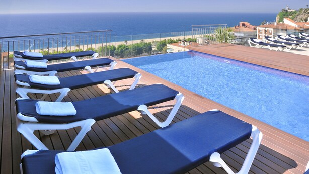 A poolside area with lounge chairs and a view of the ocean.
