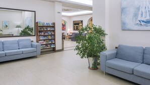 A reception area with two grey sofas, a bookshelf with magazines, a large mirror, a painting of a sailboat, and a potted plant.