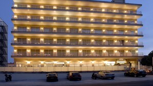A multi-story hotel with balconies, a sign reading "Hotel Catalonia," and several cars parked in front.