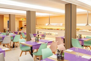 A modern restaurant with purple tablecloths, colorful chairs, and a central buffet area. - Hotel Checkin Catalonia  (Calella)