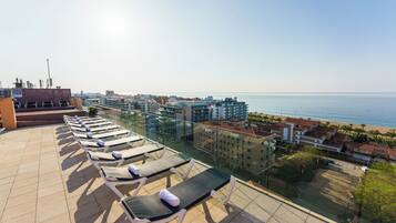 Terraza en la azotea con tumbonas y vistas al mar y al paisaje urbano.