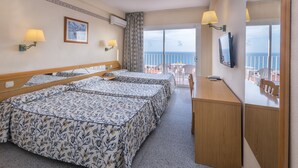 A hotel room with a balcony, two beds with floral bedspreads, a desk, and a TV.