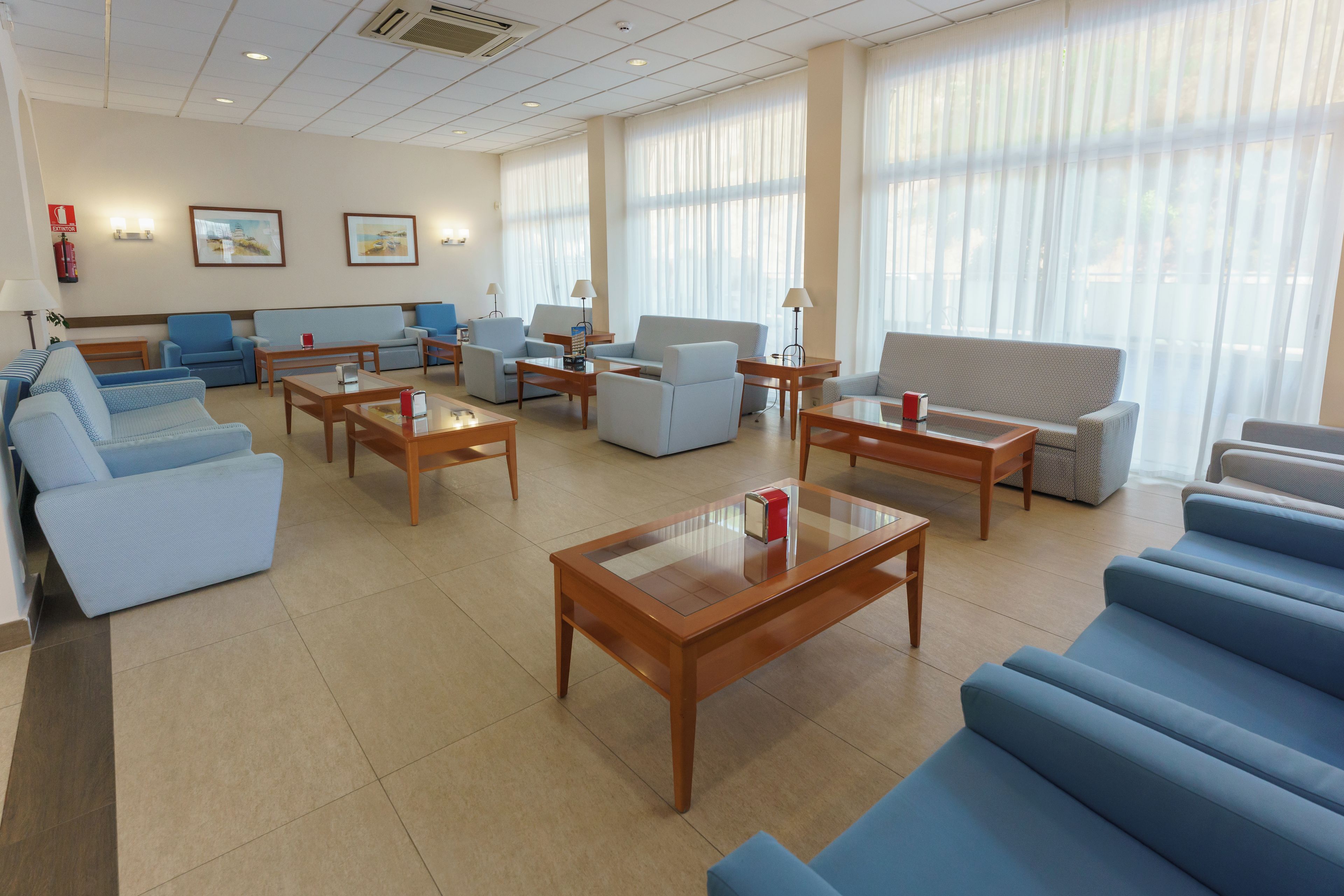 Un amplio vestíbulo de hotel con varias zonas de estar, incluyendo sofás y sillones, distribuidos alrededor de mesas de centro y una chimenea central.