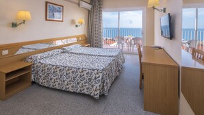 A hotel room with two beds, a desk, a chair, a TV, and a balcony with a view of the sea.