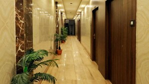 Um corredor longo e bem cuidado, com paredes de mármore, portas de madeira e plantas em vasos.
