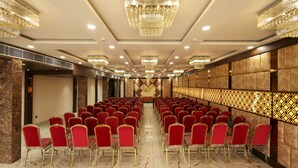 Sala de conferências com fileiras de cadeiras vermelhas, palco e lustres.