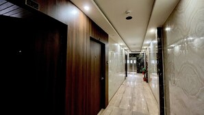 Corredor moderno de hotel com portas de madeira, paredes de mármore e teto bem iluminado.