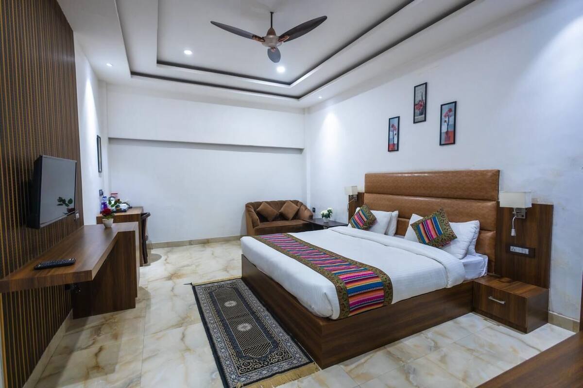 A modern bedroom with a large bed, a desk, a chair, a TV, and a ceiling fan.