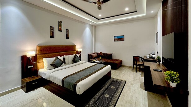 Quarto de hotel moderno com uma cama grande, um sofá, uma escrivaninha com televisão e um ventilador de teto.