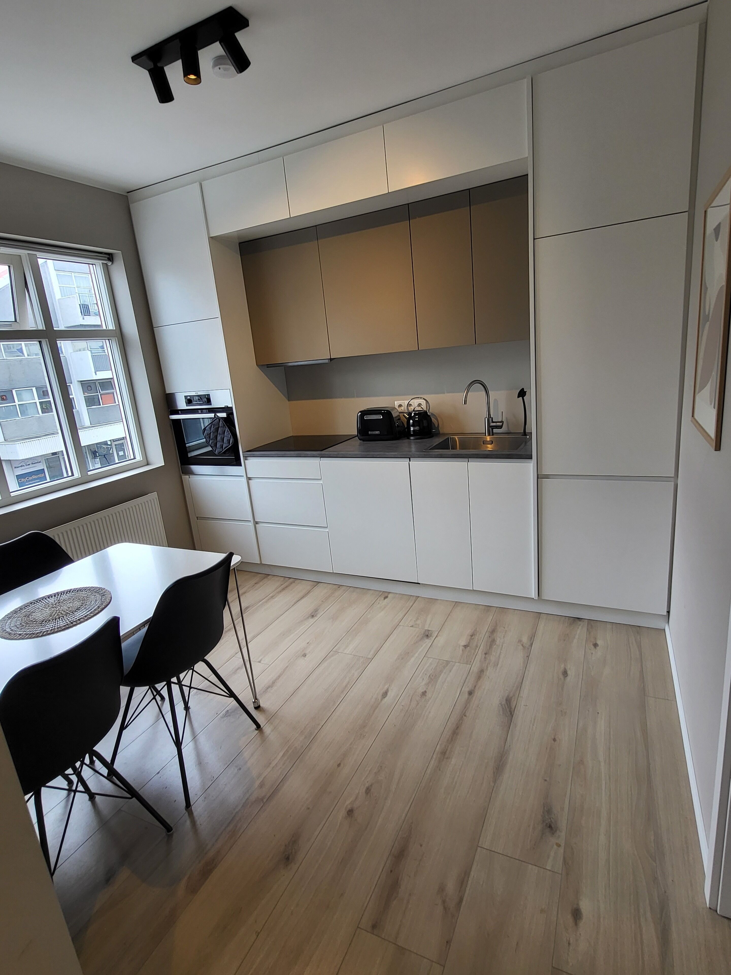 A modern kitchen with white cabinets, a built-in oven, a coffee maker, and a window overlooking a cityscape.