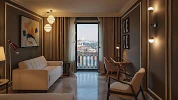 Habitación de hotel con balcón, sofá, mesa de comedor con sillas y un cuadro en la pared.
