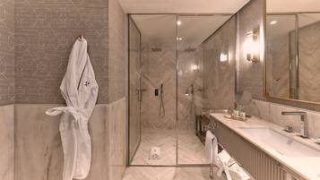 Un baño moderno con cabina de ducha de cristal, suelo de mármol en espiga y un espejo grande sobre el lavabo.