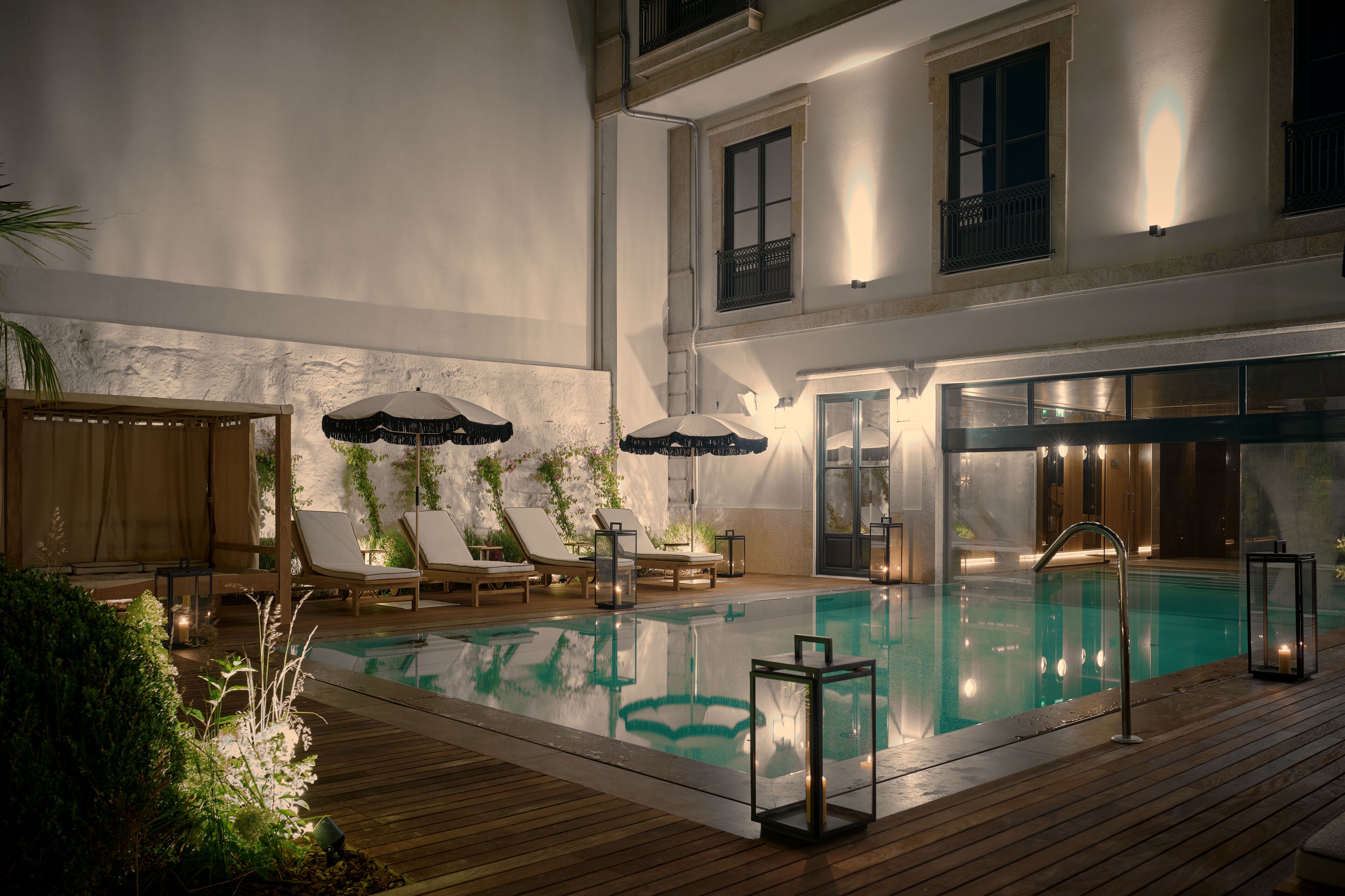 An indoor swimming pool with lounge chairs, umbrellas, and a wooden deck.