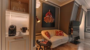 A modern living room with a sofa, a coffee machine, a table with a book, a painting on the wall, and a staircase.