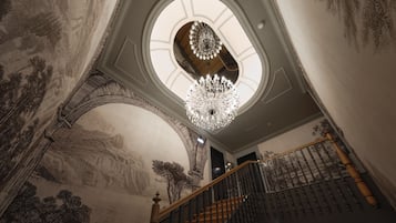 A grand staircase with a wooden handrail and black balusters, leading to a circular skylight with a chandelier.