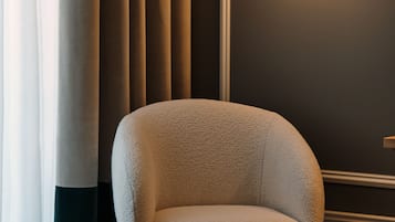 A modern chair with a textured fabric, positioned next to a wall with vertical blinds and a wall-mounted light fixture.