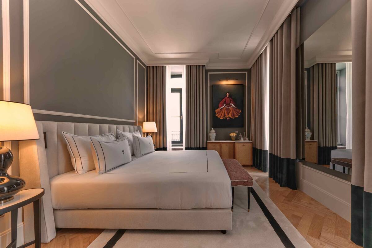A hotel room with a large bed, bedside tables, a mirror, a painting, and a view of the hallway.