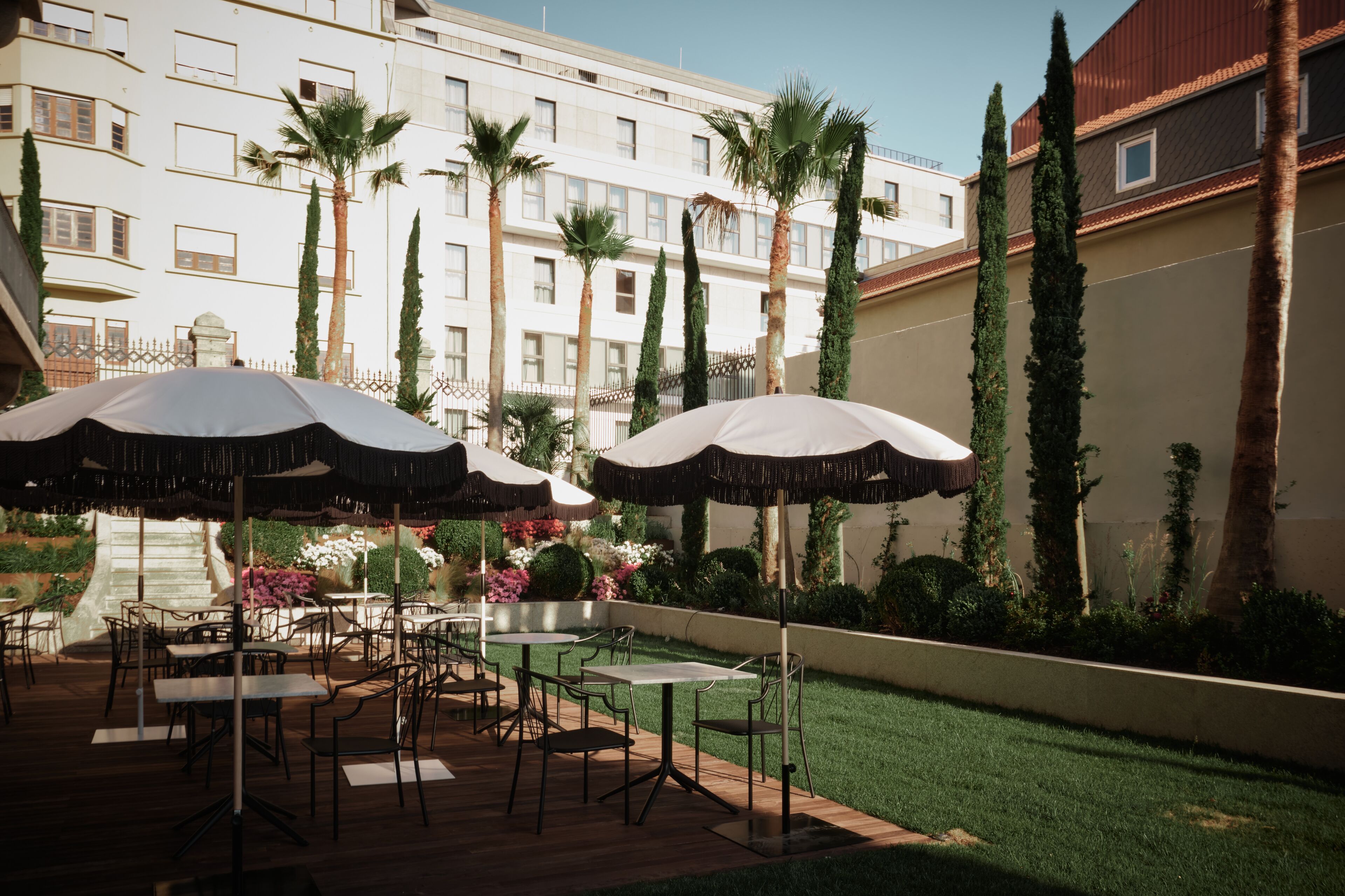 Un espace extérieur aménagé en terrasse, avec des tables et des chaises, des parasols et une vue sur un immeuble à plusieurs étages doté de balcons.