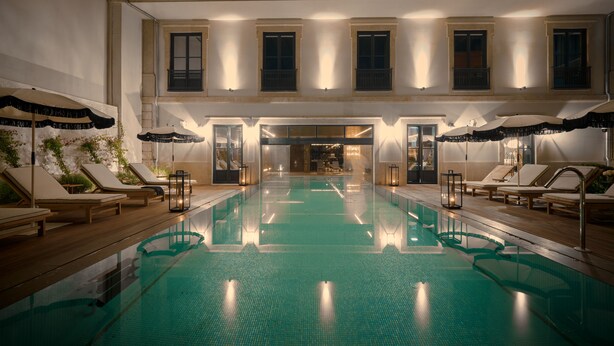 Una piscina interior con sillas de descanso y sombrillas, rodeada por un edificio de varios pisos con balcones.