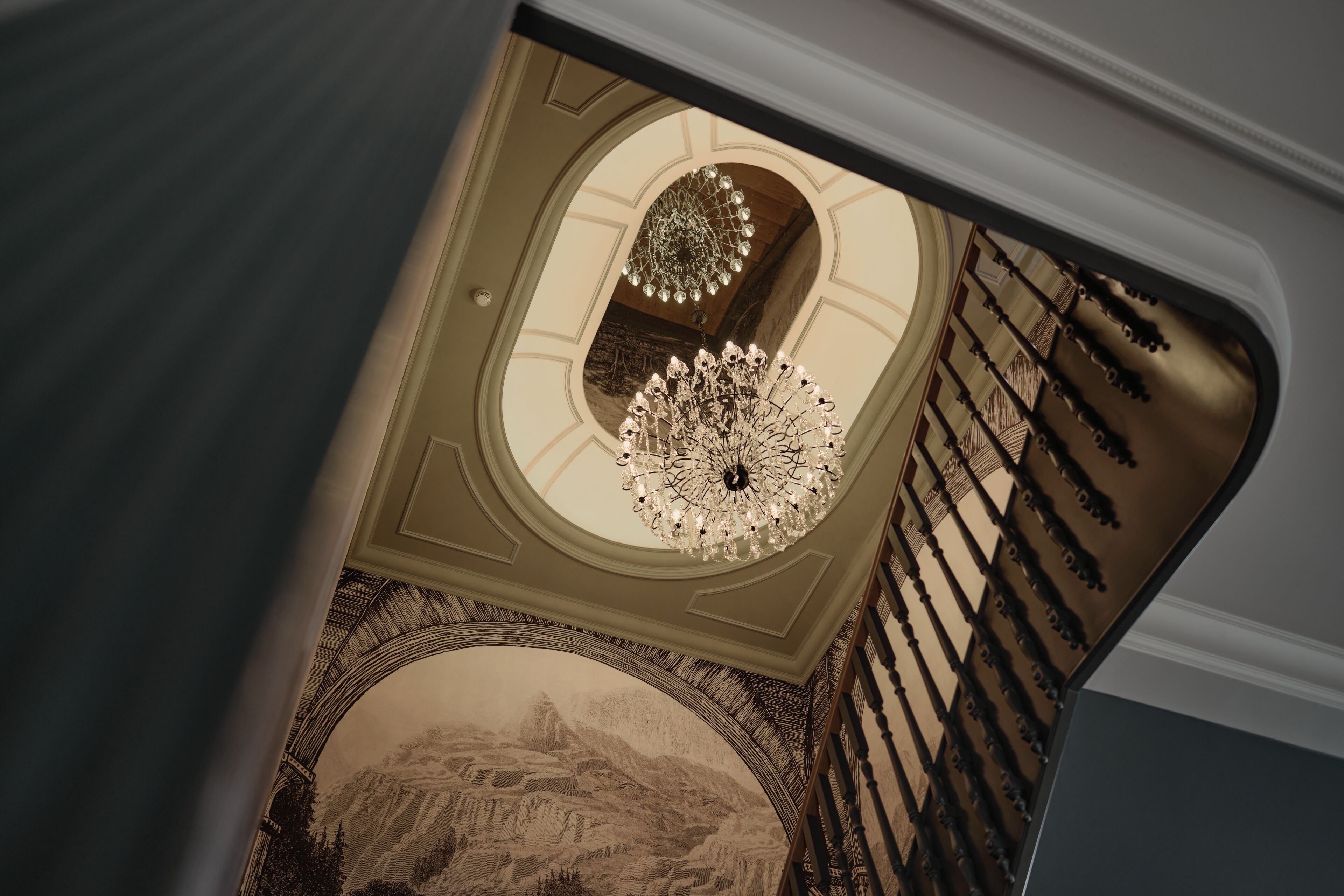 A grand staircase with a detailed mural and a chandelier.