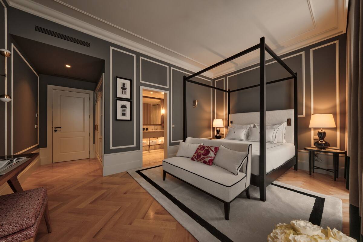 A modern bedroom with a four-poster bed, a sofa, a desk, and a reading chair.