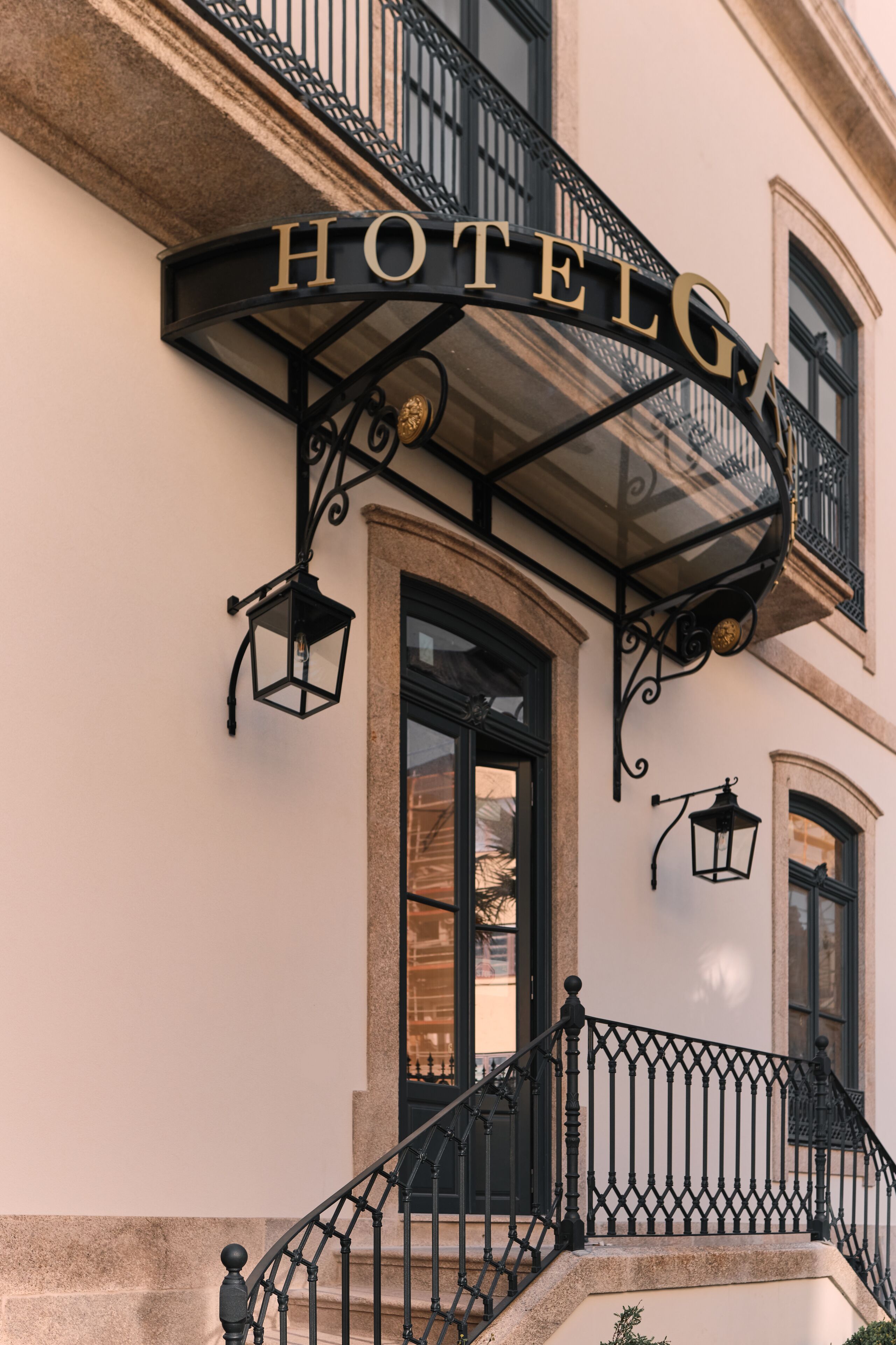 A hotel entrance with a black wrought iron balcony and a sign above the door.