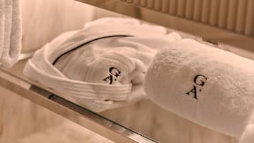 A bathroom with a glass shelf holding a white towel and a white bathrobe with embroidered initials.