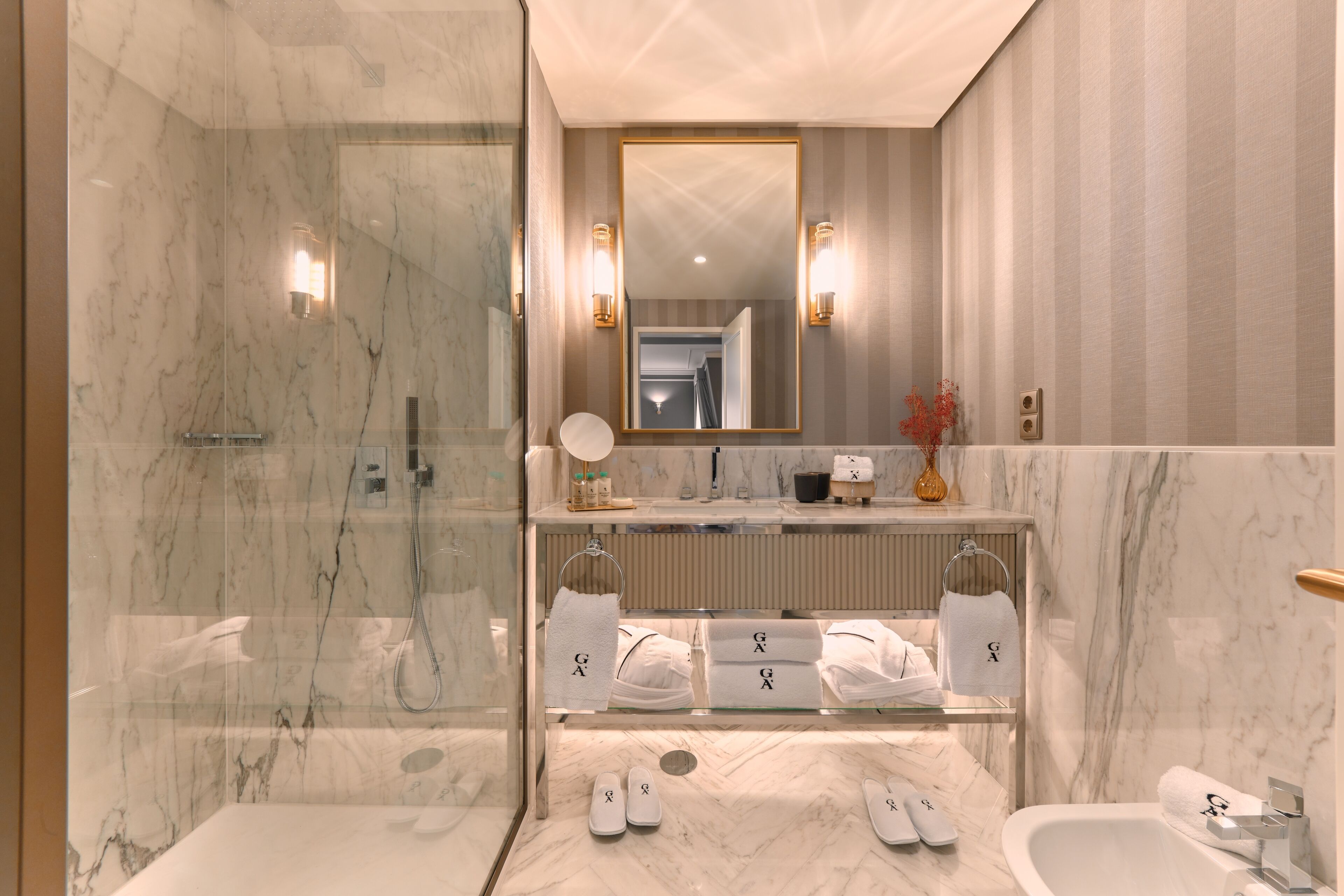 A modern bathroom with a glass-enclosed shower, a large mirror, and a vanity with multiple towel racks.