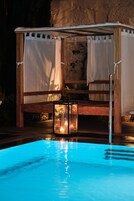 A wooden bench with a canopy, a glass lantern, and a pool with blue lighting.