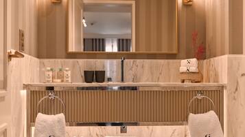 Un baño moderno con tocador de mármol, un espejo grande y estante de vidrio con toallas y zapatos.
