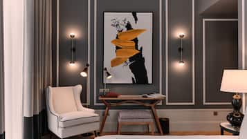 Une chambre d’hôtel moderne avec un grand lit, un fauteuil blanc, une petite table avec une lampe et un grand tableau abstrait accroché au mur.