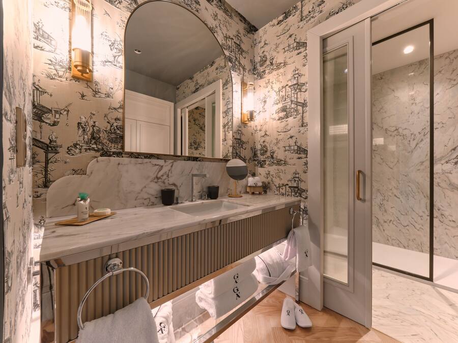 Une salle de bain moderne avec un meuble-lavabo en marbre, une douche en verre et un papier peint à motifs.
