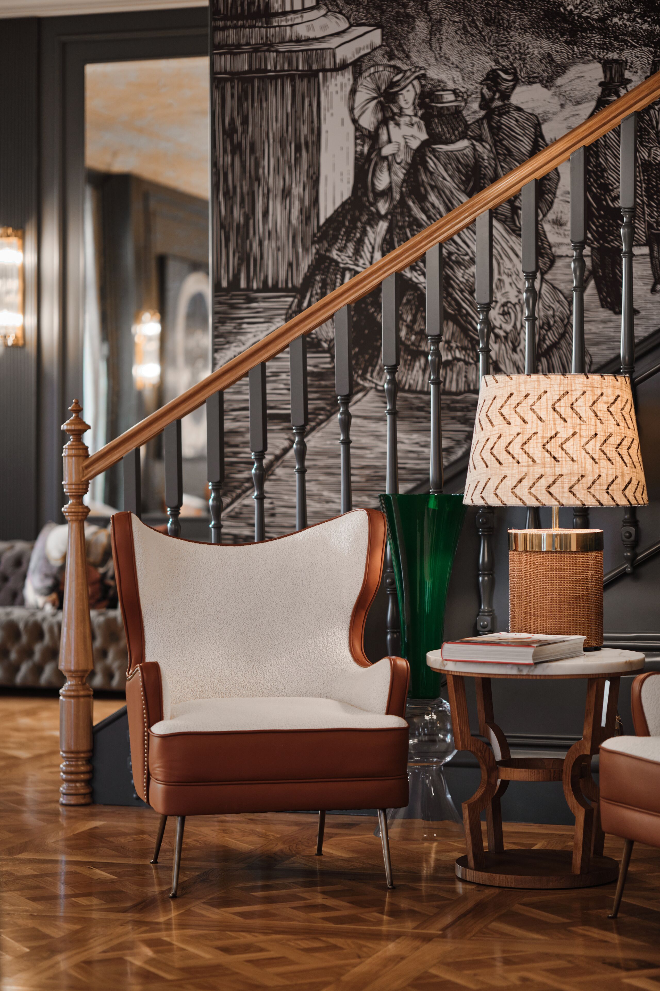 A modern living room with a wooden staircase, a leather armchair, a round table, and a lamp.