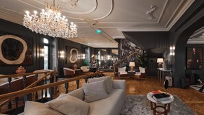 Un lobby de hotel lujoso con una gran araña, asientos cómodos, una escalera y un cuadro grande en la pared.