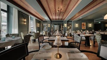 A restaurant with tables set for dining, featuring patterned ceiling and wall designs, and a chandelier.