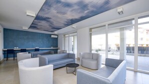 A modern lounge area with a blue accent wall, a sofa, armchairs, and a coffee table. - Opalia Residence - Eva's Elegance (Peschiera del Garda)