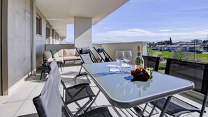 A balcony with a glass table, chairs, and a sofa. There are two wine glasses and a bouquet of flowers on the table. - Opalia Residence - Eva's Elegance (Peschiera del Garda)