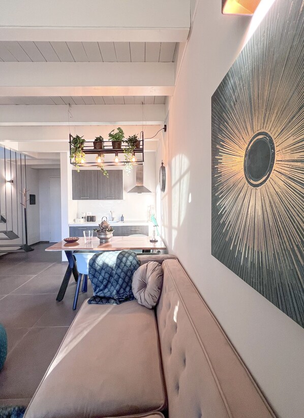 A modern living room with a large wall-mounted artwork, a sofa, and a dining area in the background.