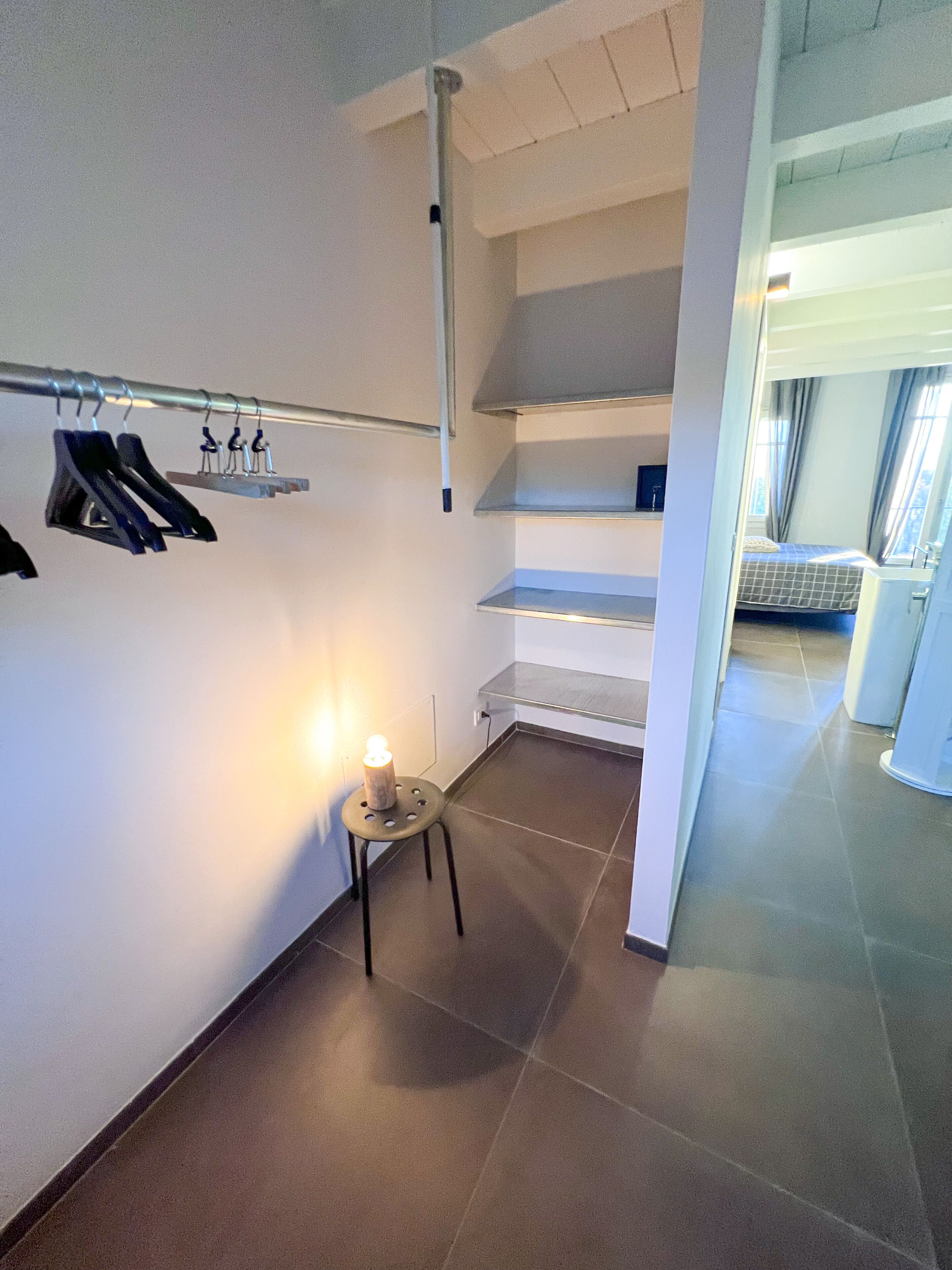 A hotel room with a bed, a small table with a candle, a coat rack, and a view of the outside through a window.
