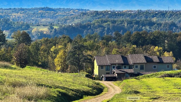 A house with a sloped roof, surrounded by a lush green landscape and a mountain range in the background. - Langhe Wine & Relax (Piemonte)