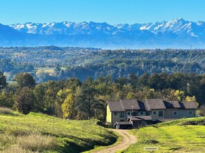 A house with a sloped roof, surrounded by a lush green landscape and a mountain range in the background.