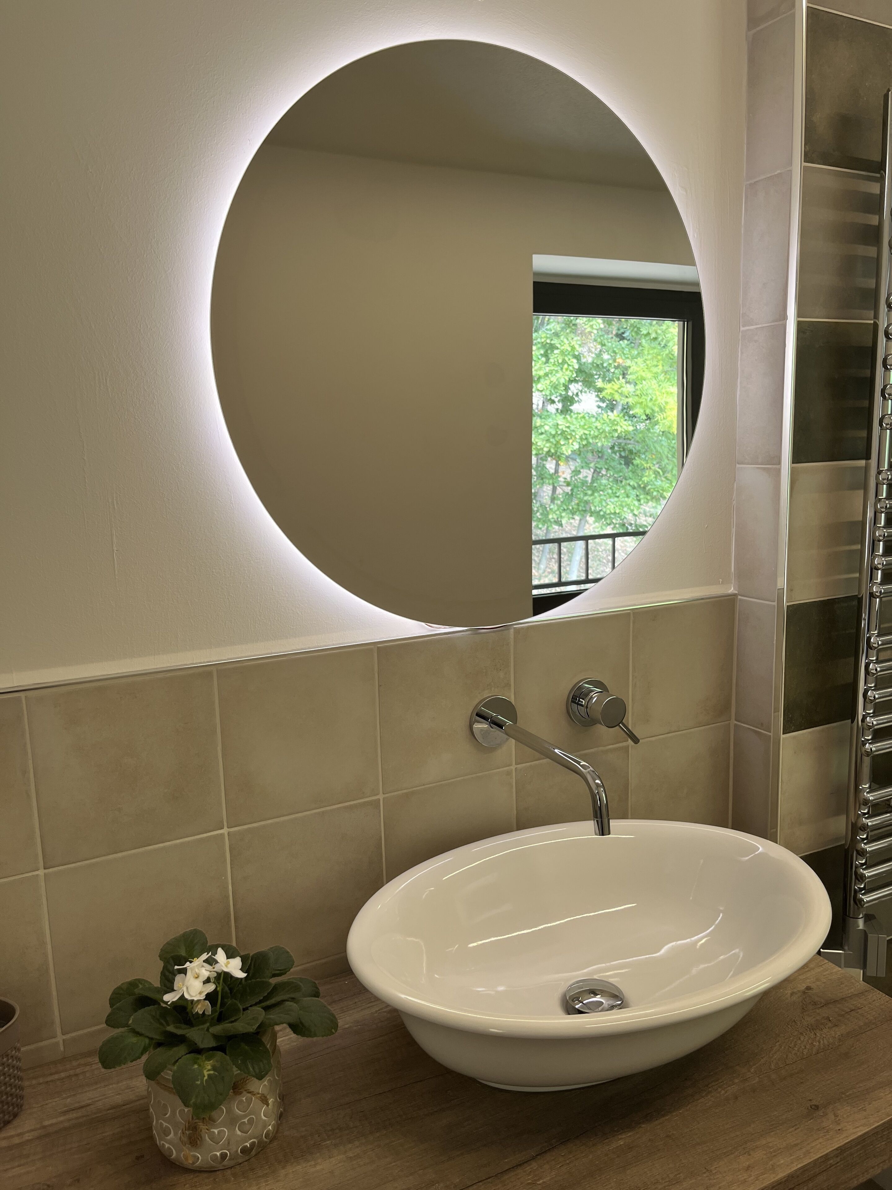 Un baño con un espejo redondo, un lavamanos blanco y una planta en maceta.