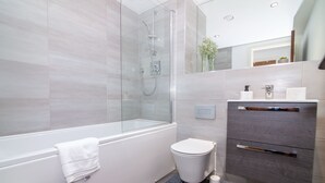 A modern bathroom with a glass-enclosed shower, a white toilet, and a grey vanity with a mirror. - Impressive Apartment in Birmingham (Birmingham)